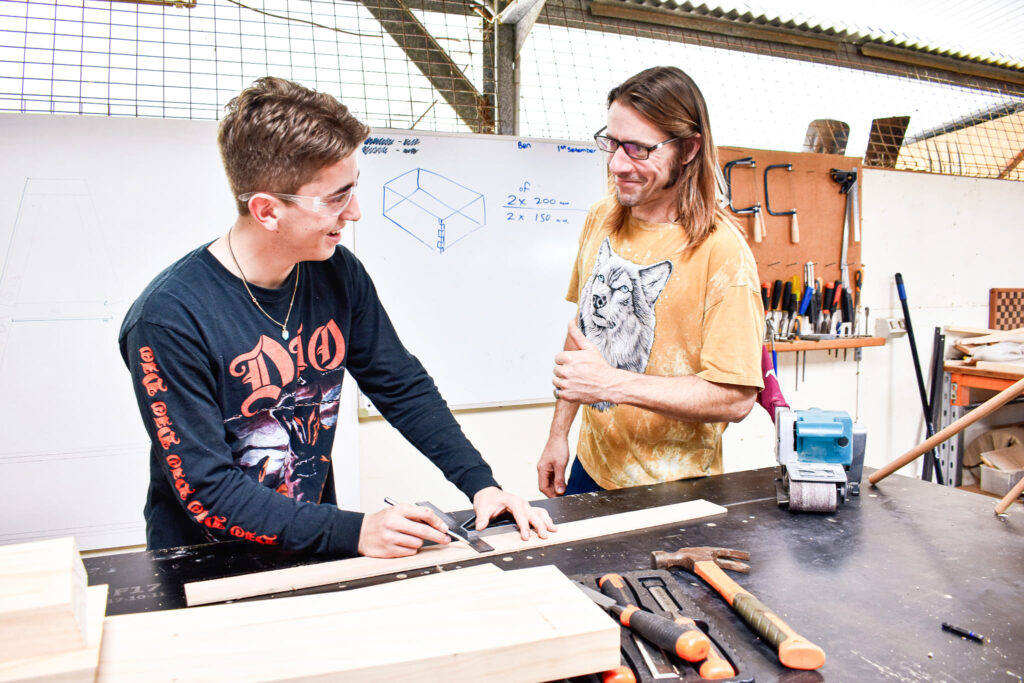 Two men discussing the measurement of wood, demonstrating an industry skill in vocational training