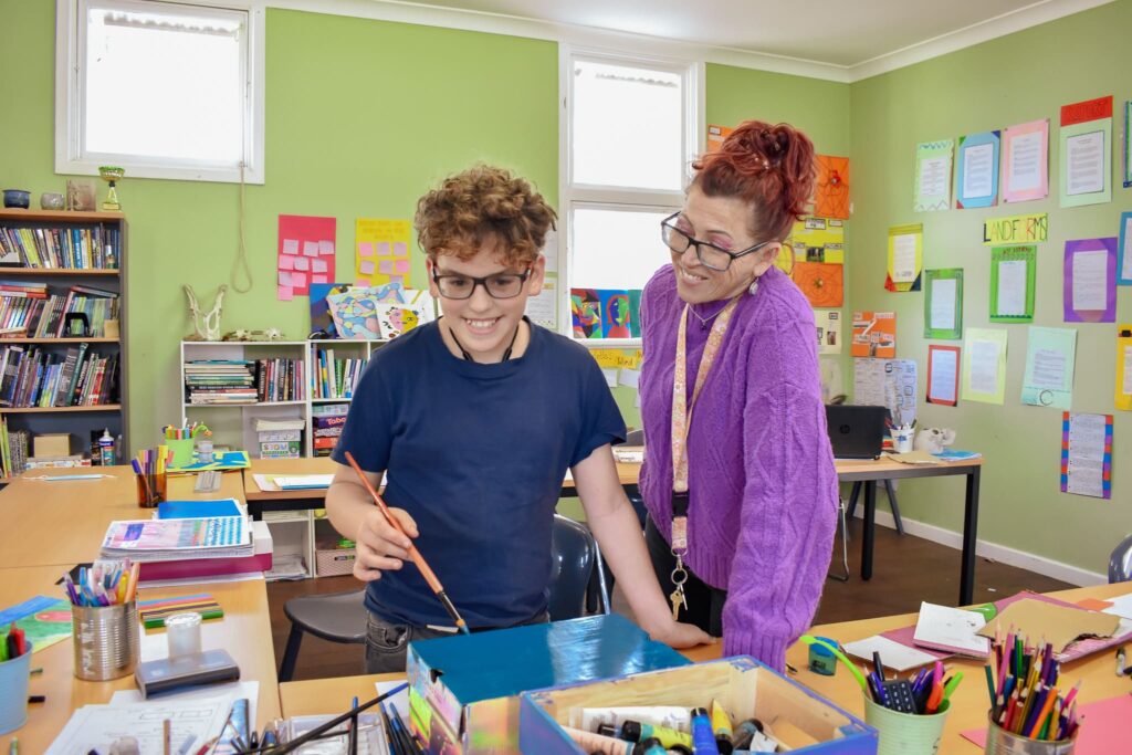 A woman portraying the critical role of a mentor in supporting student well-being during a painting activity inside a room